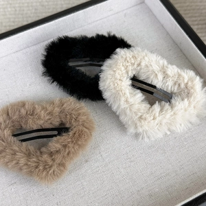 Three plush heart hair clips in black, beige, and khaki displayed on a linen tray