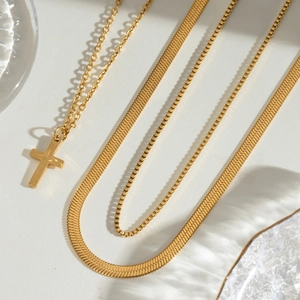 Close-up of golden necklace set with cross pendant, herringbone chain and box chain