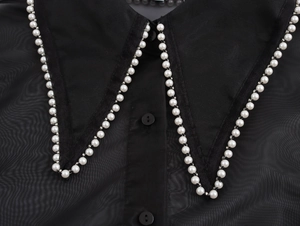 Detail of elegant black organza blouse collar with white pearl trim and buttons