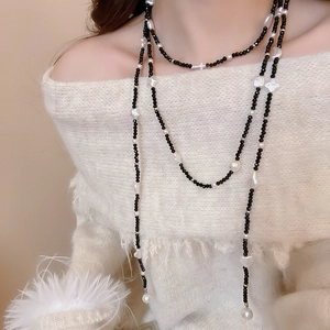 Detail of elegant layered necklace with black beads and white pearls on white sweater