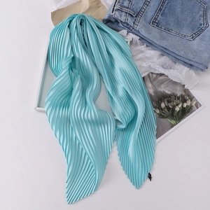 Close-up of pleated sky blue silk scarf on white table with lifestyle props