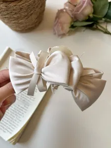 Detailed view of a creamy beige satin bow hair claw clip held against a floral background