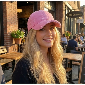 Close-up of pink distressed baseball cap with ripped details worn in an outdoor cafe setting