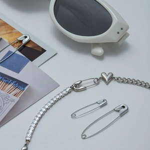 Detailed view of silver heart and safety pin pendant necklace with zircon crystals