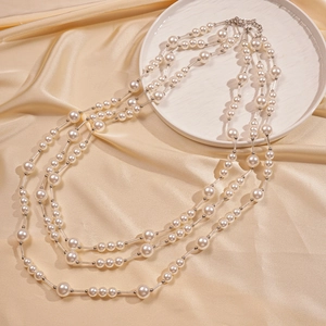 Détail d'un élégant collier de perles à trois rangs avec tubes métalliques sur soie champagne