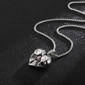 Close-up of a punk skull heart pendant featuring a red gemstone and silver box chain