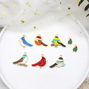 Detail of colorful enamel bird and holly leaf charms with golden borders on white tray