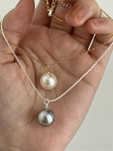 Detail of gold and silver snake chains with cream and grey pearl pendants on palm
