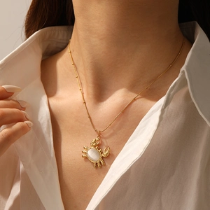 Detail of a gold crab pendant necklace with white oval stone worn on a model's neck