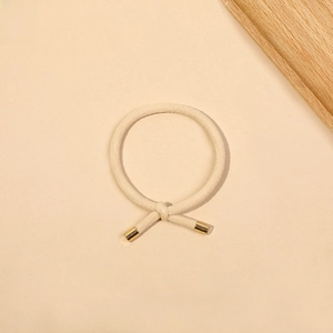 Detailed close-up of beige braided hair tie with elegant gold metallic caps on soft background