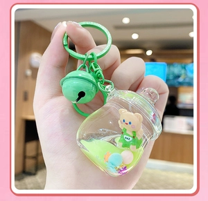 Détail d'un porte-clés bouteille avec liquide vert, petit ours et clochette colorée