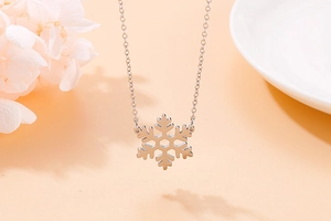 Macro shot of silver snowflake pendant necklace with delicate floral accents on pink background