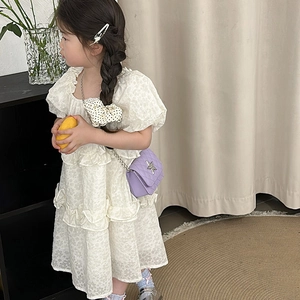 Girl wearing cream ruffled dress and purple quilted star crossbody bag in home setting