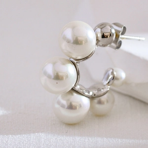 Macro shot of silver C-shaped earrings featuring elegant white pearls on fabric background