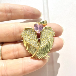 Detail view of golden angel wing pendant with clear crystals and a pink heart gem