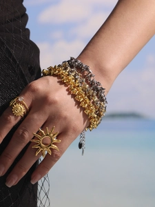 Detail of model wearing layered gold and silver heart bracelets with sun ring at the beach