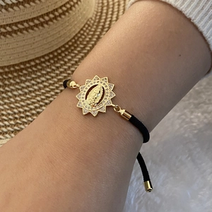 Close-up of 18K gold Virgin Mary bracelet with micro-pave zircons and black woven cord