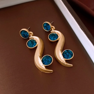 Close-up of S-shaped gold earrings set with three sparkling round blue gemstones