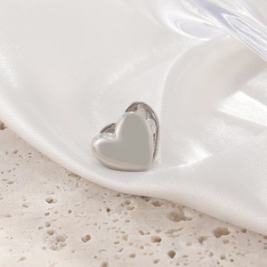 Minimalist silver heart ear cuff accessory on elegant white silk and stone surface