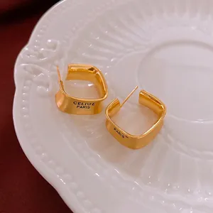 Elegant gold-plated square hoop earrings with brushed metal finish on white ceramic plate