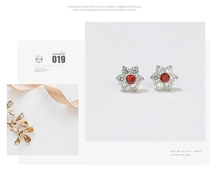 Detail of flower stud earring with red gemstone center and clear crystals on white base