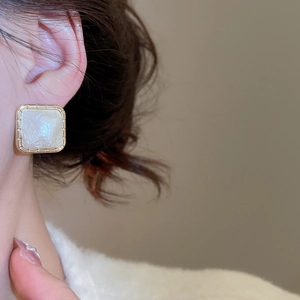 Detail of square gold-plated earrings with lustrous white inlay worn by model