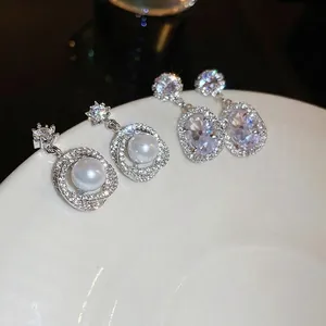Sparkling zircon flower pearl earrings with silver needles and crystal charms on white porcelain