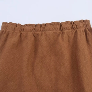 Detailed close-up of brown linen midi skirt waist with elastic shirring and fabric texture