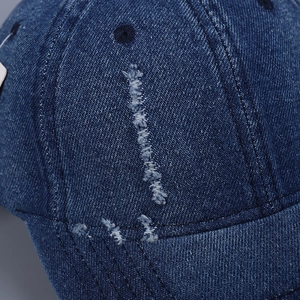 Detail of distressed dark blue denim baseball cap with frayed holes and premium stitching