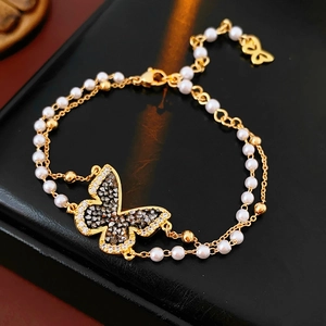 Detail of gold plated butterfly bracelet with crystal inlay and layered pearl chain