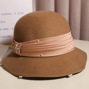 Detailed close-up of brown wool cloche hat with pink satin ribbon and pearl brooch decoration