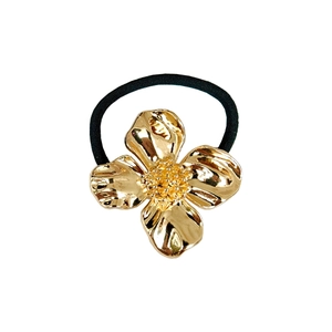 Detailed close-up of golden alloy four-petal flower hair tie with textured petals and elastic