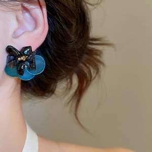 Close-up of a vintage floral earring with blue petals and black crystals on a female model