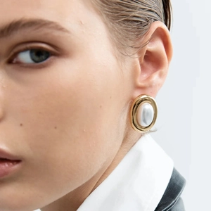 Close-up of vintage oval pearl earrings with gold metallic frame on a female model
