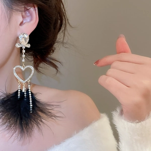 Macro detail of luxury heart earrings with black feathers and sparkling rhinestone tassels