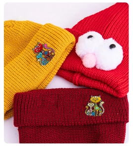 Détail de bonnets en tricot colorés avec broches chat en émail et yeux pompons blancs