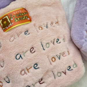 Détail macro du tissu peluche rose avec broderie 'you are loved' et étiquette de marque