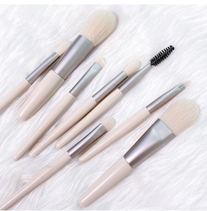 Flat lay of 8-piece portable makeup brush set with beige handles on white fur background