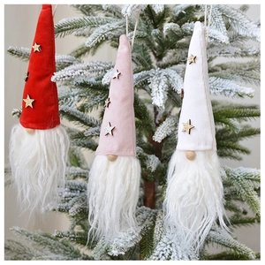 Close-up of three plush Christmas gnomes hanging on a snowy tree with glittery star hats