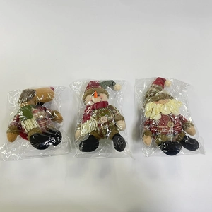 Close-up of three Christmas plush dolls with red-green plaid fabric in plastic packaging