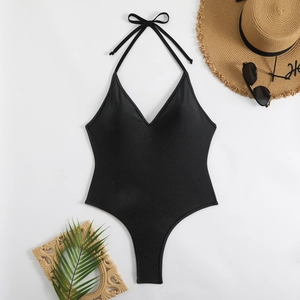 Solid black halter one-piece swimsuit with deep V-neck and high-cut leg on a beach setup