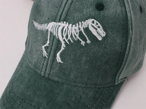 Detailed close-up of white dinosaur bone embroidery on washed green cotton baseball cap