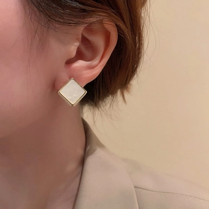 Gros plan d'élégantes boucles d'oreilles carrées dorées avec insert crème sur modèle