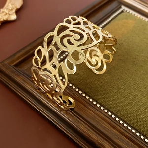 Close-up of golden hollow cuff bracelet with intricate floral rose patterns and textures