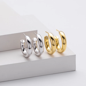 Detail view of thick polished C-shape hoop earrings in gold and silver finishes
