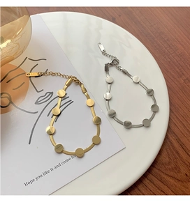 Nahaufnahme von gold- und silbernen Schlangenarmbändern mit runden Plättchen auf einem Teller