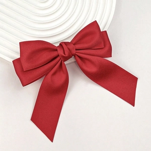 Close-up of a red satin bow hair clip with a smooth glossy finish on a white tray