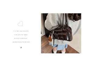 Detail of a dark brown shoulder bag with dual handles and plush ball charm accessory