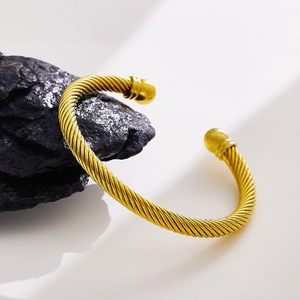 Macro detail of twisted gold cuff bracelet with spherical ends on a black rock surface