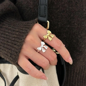 Detailed view of gold and silver bow rings worn by a model with knitwear background